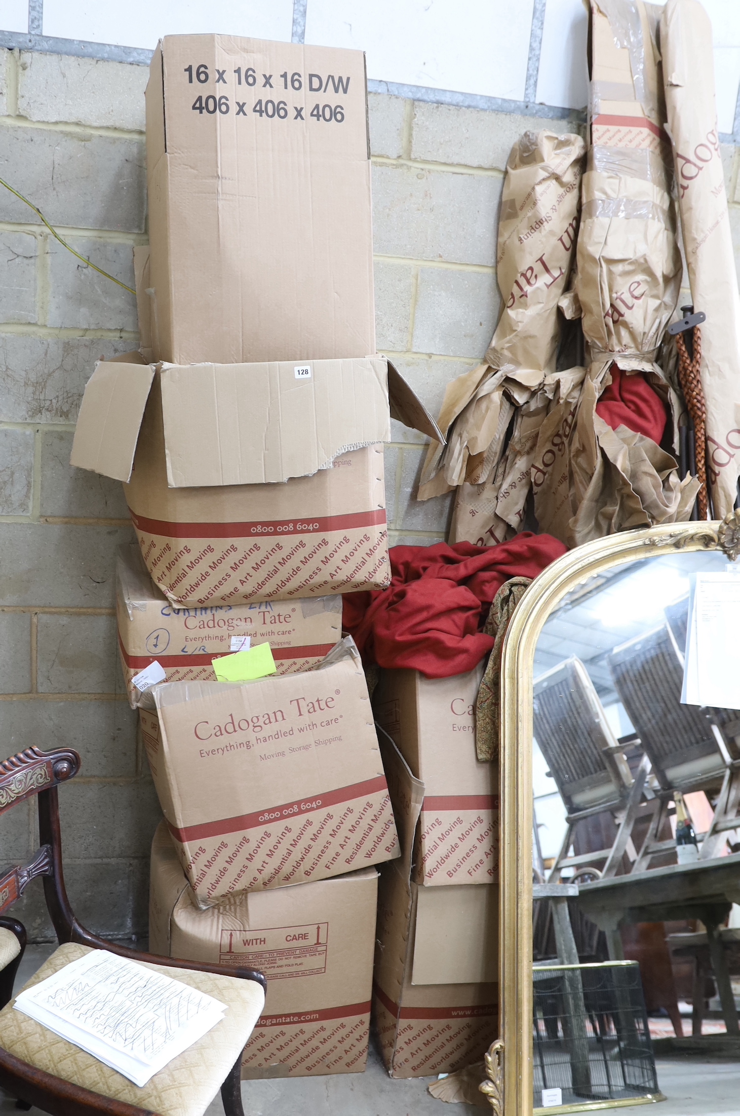 A quantity of aged metal curtain poles with woven leather tie backs and a large quantity of patterned red fabric curtains